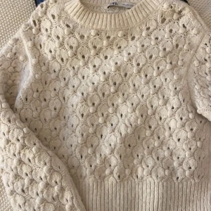 Beige stickad tröja från Zara - Mysig beige stickad tröja från Zara med ett unikt hålmönster. Perfekt för kyliga dagar med sin varma och bekväma design. Tröjan har långa ärmar och en ribbad kant vid halsen och nederdelen. Passar perfekt till både jeans och kjol!