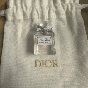 Miss Dior Blooming Bouquet parfym - Säljer en elegant och feminin Miss Dior Blooming Bouquet parfym. Flaskan är liten och fyrkantig med en söt silverfärgad rosett på korken. Kommer i en lyxig vit påse med Dior-loggan i guld. Perfekt för att ge en touch av lyx till din vardag eller som en fin present.