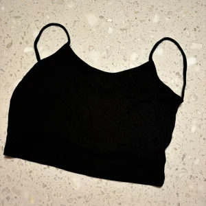 Svart ribbad linnetopp öppen rygg  - Snygg svart ribbad linnetopp med smala axelband. Perfekt för sommardagar eller som ett lager under en jacka. Enkel och stilren design som passar till allt! Öppen i ryggen med endast två band