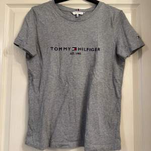 Säljer en snygg grå t-shirt från Tommy Hilfiger i storlek XS. Den har korta ärmar och ett klassiskt tryck med märkesloggan på framsidan. Perfekt för en casual look eller att matcha med jeans. Den är knappt använd.