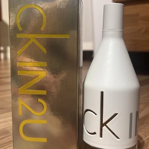 CK IN2U Her Parfym - Säljer en fräsch och modern parfym från Calvin Klein, CK IN2U Her. Flaskan är vit med en stilren design och har en genomskinlig botten. Förpackningen är guldig med stora bokstäver. Perfekt för den som gillar en ungdomlig och energisk doft! 