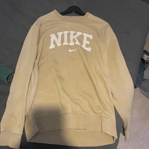 Beige sweatshirt från Nike - Säljer en snygg beige sweatshirt från Nike i storlek M. Tröjan har en klassisk design med Nike-loggan i vitt på framsidan. Perfekt för en avslappnad stil och passar bra till både jeans och träningsbyxor.