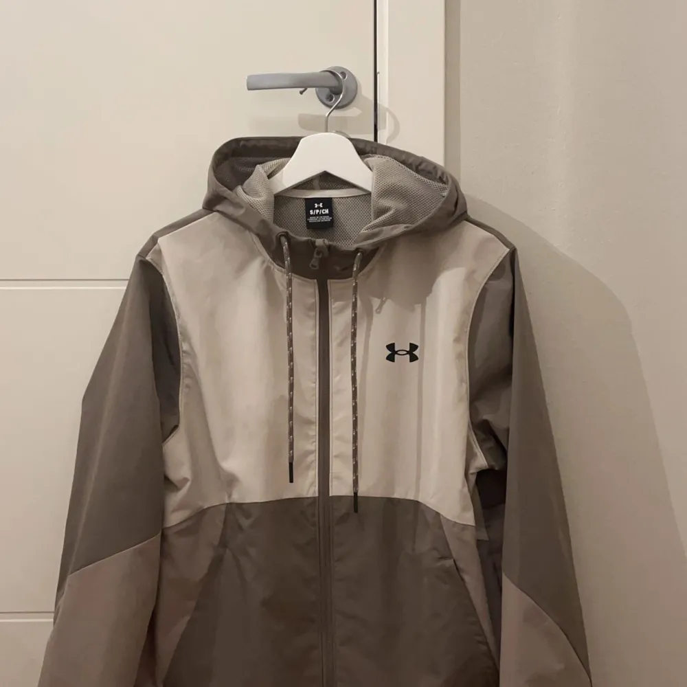 Säljer en snygg grå och beige vindjacka från Under Armour. Helt ny!. Jackor.