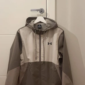 beige vindjacka från Under Armour - Säljer en snygg grå och beige vindjacka från Under Armour. Helt ny!