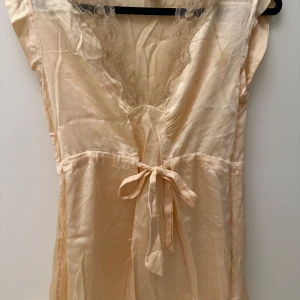 Champagnefärgad blus i siden med spetsdetaljer - Säljer en elegant champagnefärgad blus i 100% siden med vacker spets vid halsringningen. Blusen har en knytning framtill och är gjord i äkta siden som ger en lyxig känsla. Perfekt för sommarens fester eller en romantisk kväll. 💫 Passar till jeans eller byxor! Strl 36