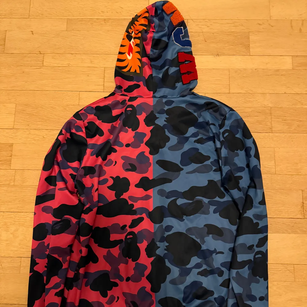 Säljer en unik hoodie med camo-mönster i blått och rosa. Den har ett coolt hajmotiv på framsidan och en dragkedja. Perfekt för att sticka ut i mängden! 🦈. Tröjor & Koftor.