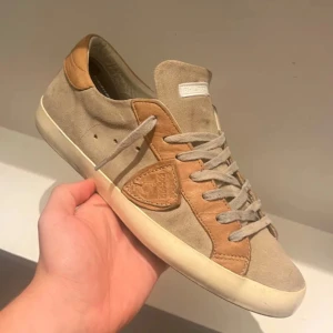 Philippe Model str 42 - Säljer ett par snygga beige sneakers från Philippe Model i mocka och skinn. De har en stilren design med snörning och en vit sula. Perfekta för både vardag och fest! Skorna är i bra skick med lite slitage på sulan. Philippe model PSRX | 42 | Skick 9/10 | Endast Skorna | Nypris 3300kr | Skriv vi frågor… Pris kan diskuteras vid snabbb affär.