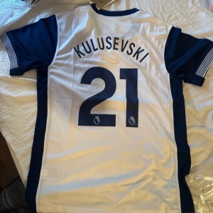 Vit och marinblå fotbollströja med Kulusevski 21 - Säljer en snygg vit och marinblå fotbollströja från Nike med Kulusevski och nummer 21 på ryggen. Tröjan har korta ärmar och klubbens emblem på bröstet. Perfekt för fans som vill visa sitt stöd! 🏆