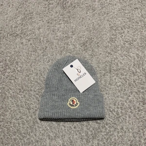 Grå ribbad mössa från Moncler - Säljer en snygg grå ribbad mössa från Moncler. Den är i nytt skick och har en broderad Moncler-logga framtill. Perfekt för kalla dagar och ger en stilren look. Passar både till vardags och mer uppklädda tillfällen. Ett måste för vintern! 🧢