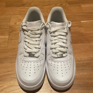 Vita Nike Air Force sneakers - Säljer ett par klassiska vita Nike Air Force sneakers i storlek herr 42. De är i nytt skick och har den ikoniska designen med snörning och perforerade detaljer för extra ventilation. Perfekta för både vardag och fest!