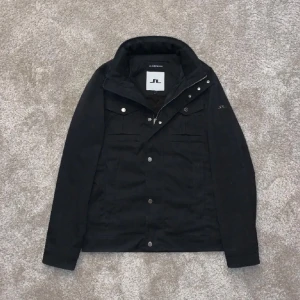 J.Lindeberg field jacka - Snygg svart jacka från J.Lindeberg i mycket bra skick. Den har en stilren design med knappar och dragkedja framtill. Perfekt för höst och vår med sin långärmade stil. Passar både till vardags och lite finare tillfällen.