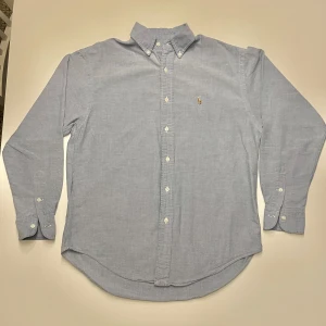 Ljusblå skjorta från Ralph Lauren - Säljer en klassisk ljusblå skjorta från Ralph Lauren i 100% bomull. Skjortan har en broderad logga på bröstet och knappar hela vägen ner. Perfekt för både vardag och fest! 🕺