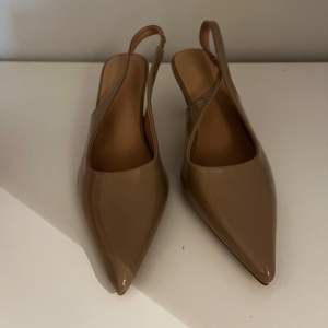 Säljer ett par oanvända eleganta beige pumps med spetsig tå och klack. Perfekta för både fest och vardag. De har en stilren design med en smidig rem runt hälen för extra komfort. Passar till många olika outfits och tillfällen!