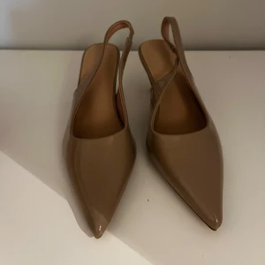 Beige pumps med spetsig tå - Säljer ett par oanvända eleganta beige pumps med spetsig tå och klack. Perfekta för både fest och vardag. De har en stilren design med en smidig rem runt hälen för extra komfort. Passar till många olika outfits och tillfällen!