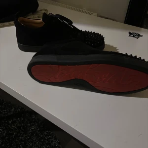 Svarta sneakers med nitar - Säljer ett par svarta sneakers från Christian Louboutin i mocka med coola nitar på ovansidan. Skorna har den ikoniska röda sulan och är i mycket bra skick. Perfekta för att ge din outfit en edgy touch!