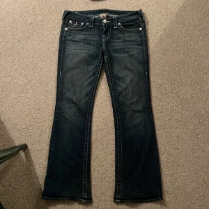 Blå lågmidjade jeans från True Religion! - Säljer ett par snygga blå lågmidjade bootcut jeans från True Religion i bra skick (liten slitning längst ner på benen). Jeansen är i storlek 29. Köpta för 900kr!