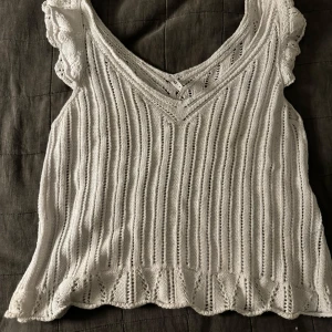 Vit stickad topp med volangdetaljer - Säljer en superfin vit stickad topp med v-ringning och volangdetaljer vid ärmarna. Perfekt för sommardagar eller på helger!!
