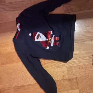 Svart jultröja med tomtemotiv från H&M - Säljer en svart jultröja från H&M med ett glittrigt tomtemotiv på framsidan. Perfekt för julfirandet! Tröjan har långa ärmar och är i bra skick. Passar utmärkt för att sprida julstämning 🎅✨