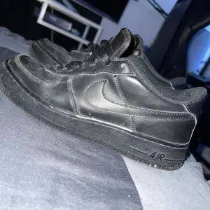 Säljer ett par svarta Nike Air Force sneakers i bra skick. De har en klassisk design med snörning och är tillverkade i skinn. Perfekta för vardagsbruk och ger en stilren look. Det finns lite slitage på insidan, men de är fortfarande bekväma att använda.