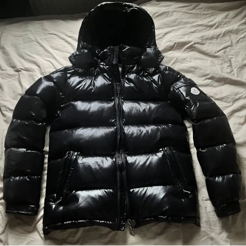 Vid snabb affär (SÄNKER PRISET).                                   Säljer en snygg svart pufferjacka från Moncler i mycket bra skick. Jackan har en glansig finish och är perfekt för kalla vinterdagar. Den har en dragkedja framtill och en huva för extra värme. Moncler-loggan syns tydligt på ärmen. Perfekt för dig som vill hålla stilen även när det är kallt ute!. Jackor.