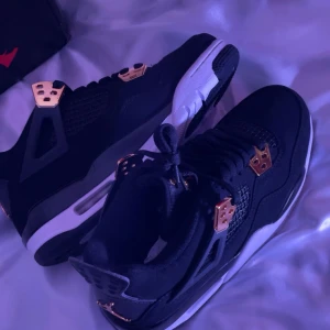 Svarta sneakers med gulddetaljer - Snygga svarta jordan 4 med gulddetaljer och vit sula. Perfekta för att ge din outfit en lyxig touch. De har snörning och är i mycket bra skick. Passar både till vardags och fest! 