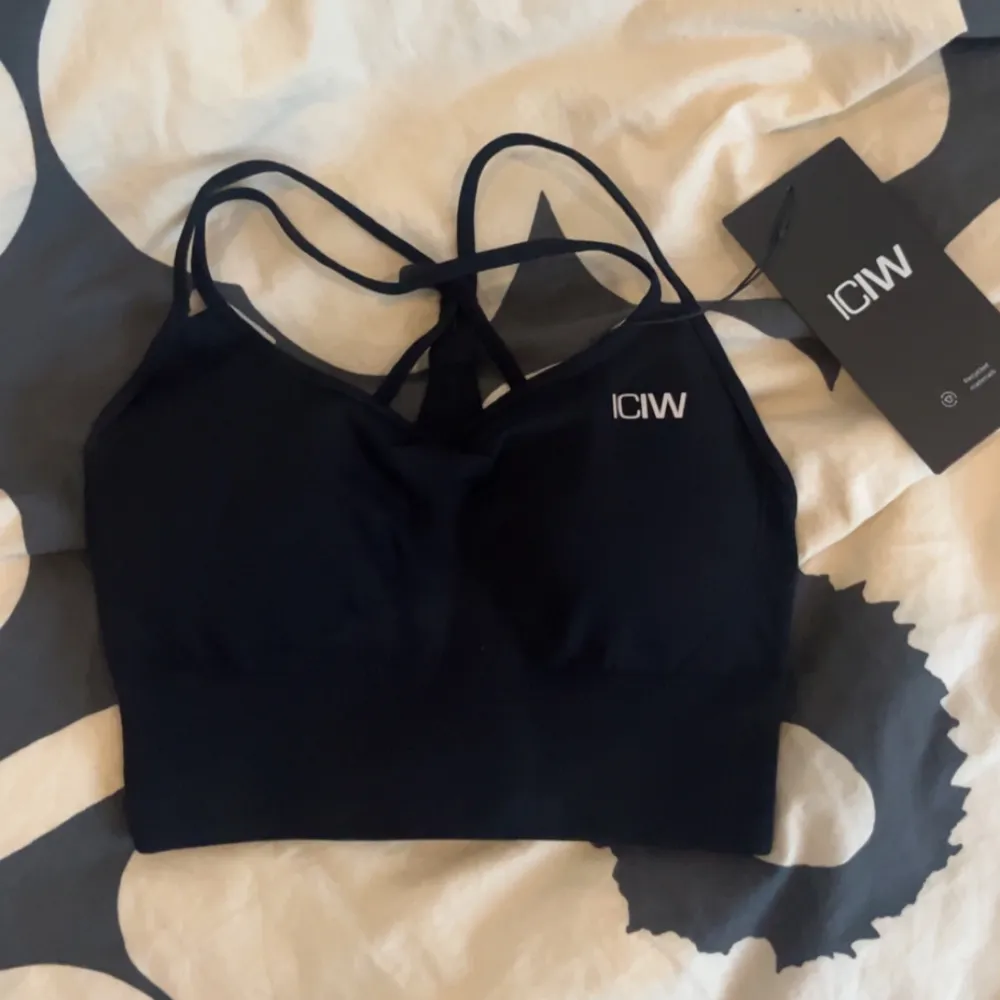 Säljer en svart sömlös sport-bh från ICANIWILL i storlek XS. Den har ett reflekterande logotyptryck fram och är tillverkad av 92% återvunnen nylon och 8% spandex. Bh:n har 4-vägs stretch och avtagbara kupor för låg support. Perfekt för träning!. Toppar.