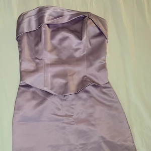 Ljuslila axelbandslös klänning - Säljer en elegant ljuslila axelbandslös klänning i satin. Perfekt för festliga tillfällen med sin stilrena design och glansiga yta. Klänningen har en tight passform som framhäver figuren och en vacker drapering upptill. Ett måste för garderoben om du vill glänsa på nästa event! 💜