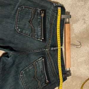 Mörkblå jeans från Diesel - Säljer ett par snygga mörkblå jeans från Diesel i bra skick. De har en klassisk femficksdesign med coola dragkedjor på bakfickorna. Jeansen är av hög kvalitet och har en bekväm passform. Perfekta för både vardag och fest!