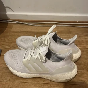 Vita Adidas Ultraboost - Säljer ett par vita Adidas Ultraboost i bra skick. De är superbekväma och perfekta för både träning och vardagsbruk. Skorna har en snygg och stilren design med snörning och den klassiska Boost-sulan för extra komfort. Passar perfekt för dig som vill ha både stil och funktion.