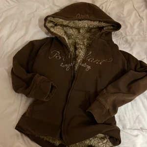 Päls zipup-hoodie  - Mysig brun zipup-hoodie med päls och broderad text på framsidan. 