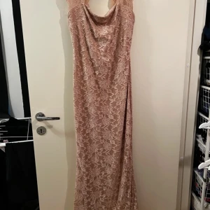 Champagnefärgad spetsklänning - Elegant långklänning i champagnefärgad spets med vackra blommönster. Klänningen har en draperad halslinje och är ärmlös, perfekt för festliga tillfällen. Materialet är mjukt och följsamt, vilket ger en bekväm passform. Den är även stretchig och i storlek 8/38. Klänningen är endast använd vid 2 tillfällen och är i mycket bra skick 