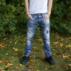 Blå slitna jeans från jack and Jones  - Vi säljer ett par snygga blå jeans med slitningar för en cool och avslappnad look. De har en klassisk femficksdesign och är perfekta för vardagsbruk. Jeansen har en normal passform och är i ett välanvänt skick, vilket ger dem en unik karaktär.
