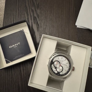 Klocka från GANT W10581 - Säljer en silverfärgad klocka från GANT. Klockan har en detaljerad urtavla med svarta och röda accenter samt robust metallarmband. Kommer i originalförpackning med extra länkar för justering. Manual och ”äkthetsbevis” finns. Diametern är 45 mm. Klo