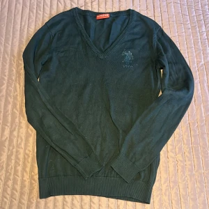 Mökblå tröja från U.S. Polo Assn. - Säljer en snygg mörkblå tröja från U.S. Polo Assn. med v-ringning och deras klassiska logga på bröstet. Tröjan är i ett mjukt material och har långa ärmar med ribbade muddar. Perfekt för både vardag och lite finare tillfällen. Passar bra till jeans eller chinos!