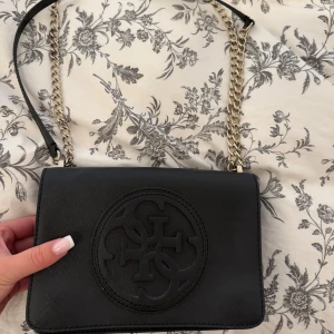 Svart Guess väska ÄKTA - En otroligt fin väska där du får plats med mobil, laddare, sminkprodukter och plånbok. Så fin väska som tyvärr inte kommer till användning.