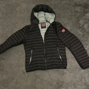Svart pufferjacka från Colmar - Säljer en snygg svart pufferjacka från Colmar i storlek 46. Jackan har en stilren design med dragkedja och huva, perfekt för kyliga dagar. Den är quiltad och har en grå insida som ger en fin kontrast. Passar perfekt för höst och vinter!