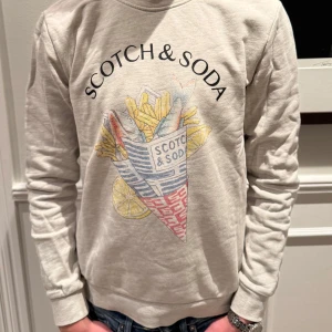 Beige sweatshirt från Scotch & Soda - Säljer en snygg beige sweatshirt från Scotch & Soda med ett coolt tryck på framsidan. Tröjan har långa ärmar och är i mycket bra skick. Det är en riktigt skön tröja för vardagen, hör av dig vid intresse samt frågor, pris är ej hugget i sten🤩🤩modellen på bilden är 168 cm 52 kg👌🏼👌🏼
