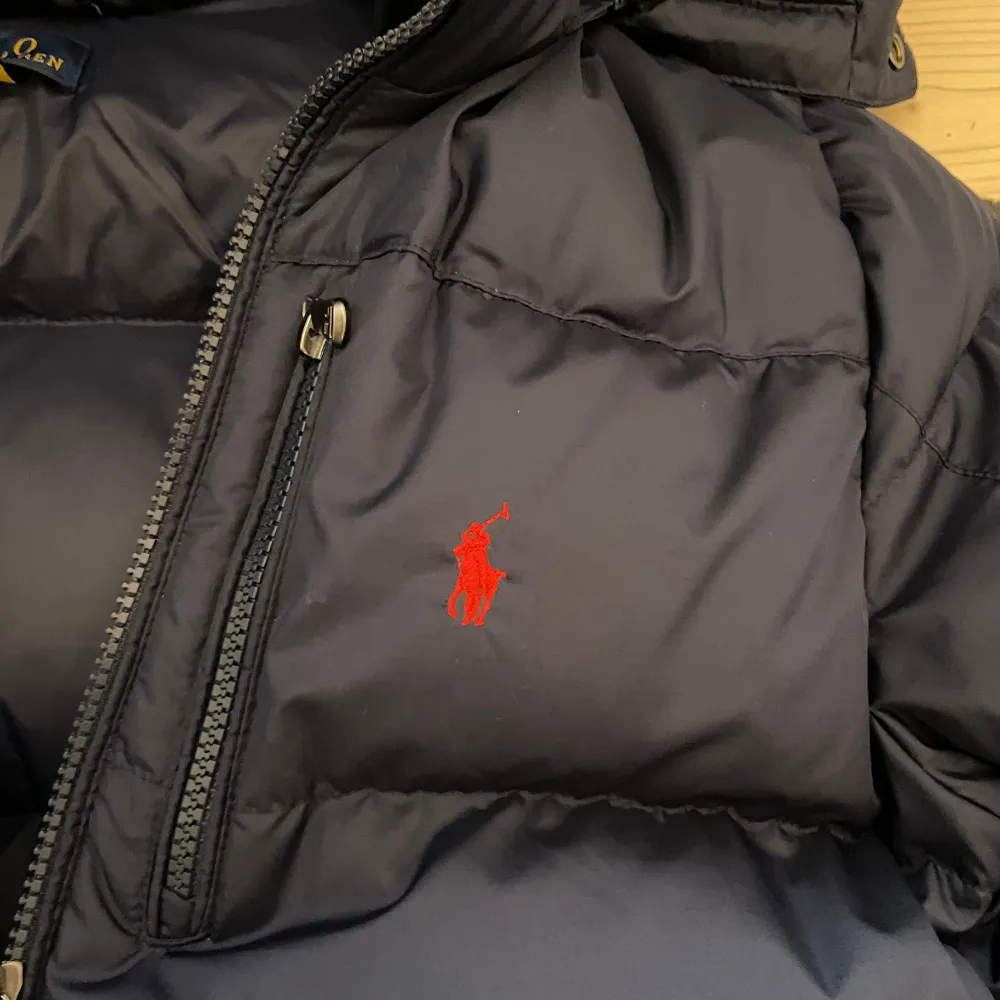 Säljer en snygg mörkblå dunjacka från Polo Ralph Lauren storlek Barn L men passar XXS runt 165-175. Jackan har en praktisk huva och dragkedja framtill. Den är perfekt för kalla dagar och har en klassisk design med det ikoniska röda Polo-logotypen på bröstet. Perfekt för vintern! ❄️. Jackor.