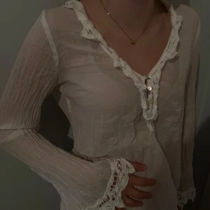 Vit långärmad blus med spetsdetaljer - Säljer en superfin vit blus med långa ärmar och v-ringning. Den har snygga spetsdetaljer vid halsen och ärmsluten, vilket ger en romantisk touch. Perfekt för både vardag och fest! 💫