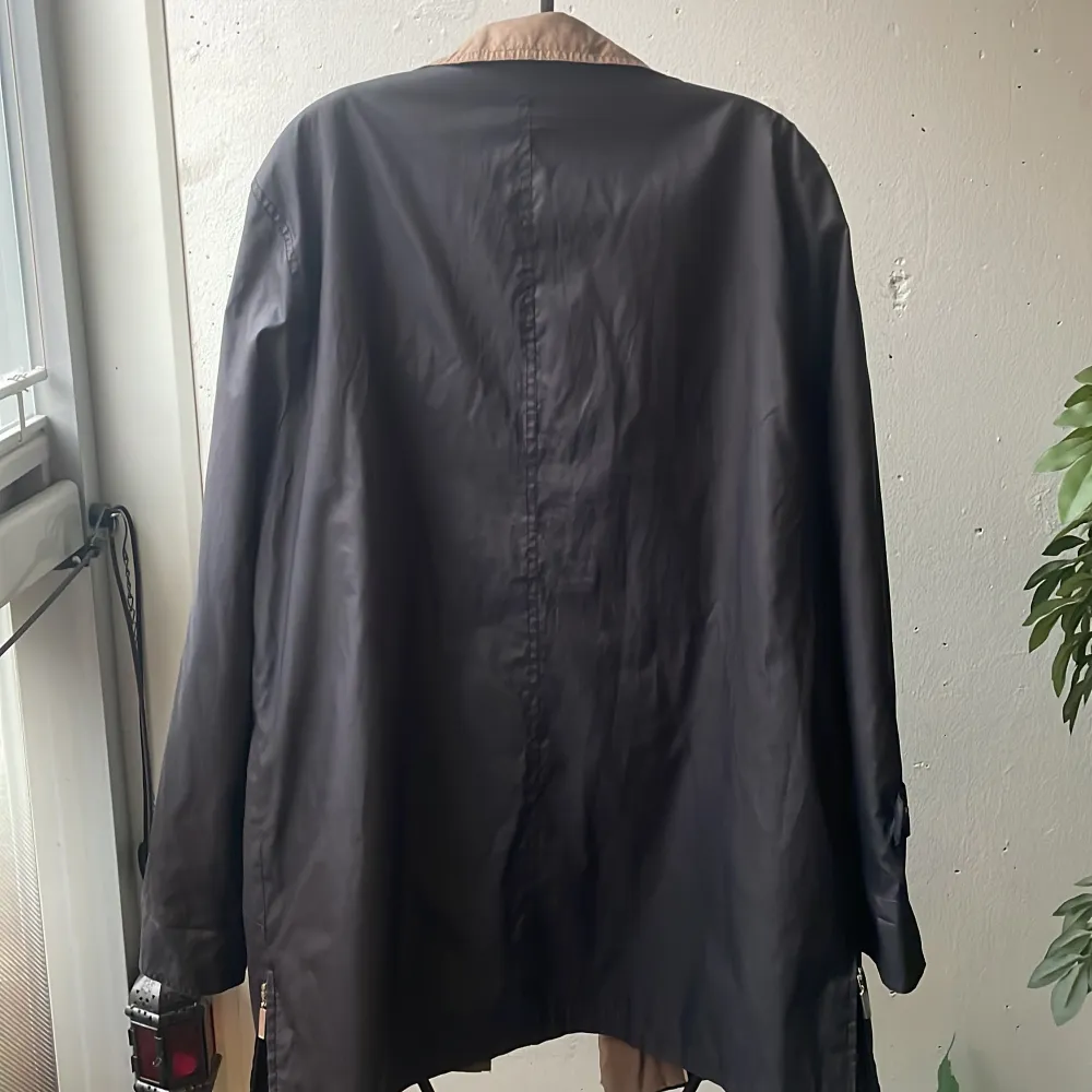 Snygg blå vind jacka från Atelier Création med brunt foder och krage. Jackan har knappar och dragkedja, samt praktiska fickor med knappar. Perfekt för höst och vår!. Takit.