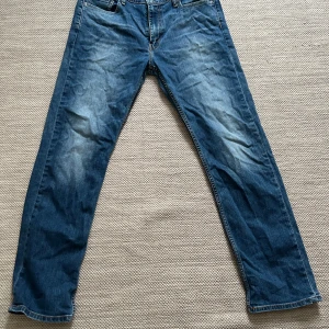Levi's blå jeans 504 - Säljer ett par klassiska blå Levi's jeans i bra skick. W36/L34 de har en straight passform och är perfekta för vardagsbruk. Jeansen har en snygg slitning framtill och är tillverkade i slitstarkt denim. Perfekta för både höst och vår!