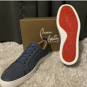 Blå sneakers från Christian Louboutin - Säljer ett par snygga blå sneakers från Christian Louboutin i mocka. De har den ikoniska röda sulan och snörning framtill. Perfekta för både vardag och fest! Skorna är i mycket bra skick och allt og medföljer