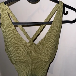 Olivgrön stickad topp - Säljer en superfin olivgrön stickad topp med korsade band i ryggen. Perfekt för sommardagar eller som ett lager under en jacka. Toppen är i ett mjukt och stretchigt material som ger en bekväm passform. Passar både till vardags och fest! Storlek S men känns som en XS