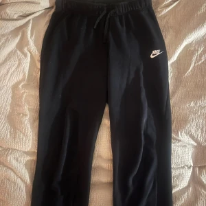 Svarta mjukisbyxor från Nike - Säljer ett par svarta mjukisbyxor från Nike i bra skick. De har en bekväm passform med dragsko i midjan för justerbarhet. Perfekta för avslappnade dagar eller träning. Nike-loggan är tryckt i vitt på ena benet.