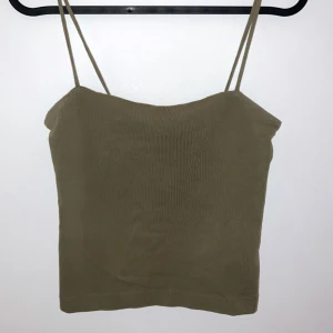 Olivgrön ribbad linnetopp - Säljer en snygg olivgrön ribbad linnetopp med smala axelband. Perfekt för sommardagar eller som ett lager under en jacka. Toppen är i bra skick och har en croppad passform som ger en trendig look. Passar till både vardag och fest!