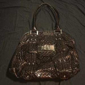 Guess väska  - Äkta Guess väska ganska stor, tyvärr har materialet lossnat på en del ställen men väskan fyller fortfarande sin funktion och ser bra ut 