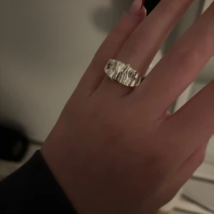 Silverfärgad ring med vågig design - Snygg och stilren silverfärgad ring med en unik vågig design. Ringen är justerbar.