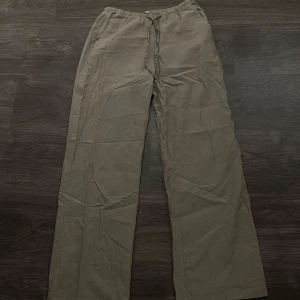 Lågmidjade beige linnebyxor med dragsko  - Säljer ett par bekväma och luftiga beige linnebyxor. De har en loose passform och är perfekta för varma sommardagar. Byxorna har en praktisk dragsko i midjan för justerbar passform. Perfekta för en avslappnad stil eller stranddagar. 