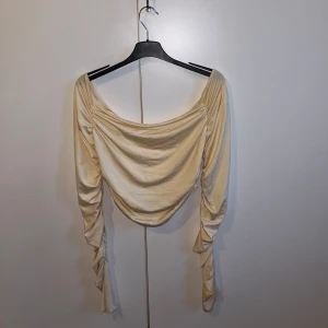 Beige offshoulder topp från Shein - Snygg beige offshoulder topp från Shein med långa ärmar och en tight passform. Toppen är croppad och har en stilren design som passar perfekt till både vardag och fest. Materialet är mjukt och stretchigt för en bekväm känsla.