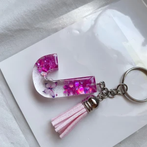 Handmade resin Nyckelring med rosa glitter och tofs💕 - Superfin nyckelring med en bokstav i rosa  glitter. Den har små fjäril  inuti och en söt rosa tofs som hänger bredvid. Perfekt som en personlig accessoar eller present💕